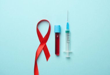 Kırmızı AIDS Farkındalık Kurdelesi, şırınga ve kan testi tüpü mavi arka planda