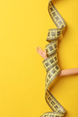 Sarı arka planda mezurası olan bebek elleri. Kilo kaybı, diyet konsepti