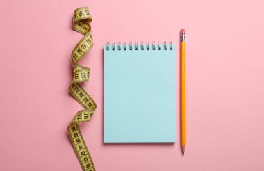 Pembe arka planda kalem ve bant ve defter ölçümü. Kilo kaybı, diyet konsepti