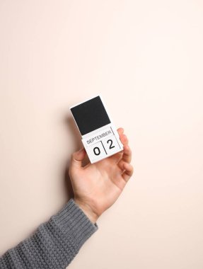 Süveter giymiş bir adamın elinde, arka planda 2 Eylül tarihli blok takvimi var.