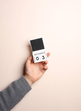 Süveter giymiş bir adamın elinde blok takvimi var. Arka planda 3 Eylül tarihi var.