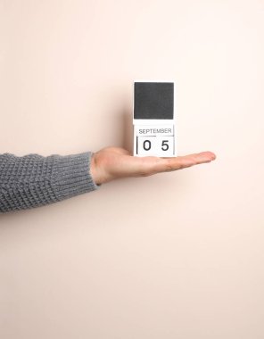 Süveter giymiş bir adamın elinde, bej arka planda 5 Eylül tarihli blok takvimi var.