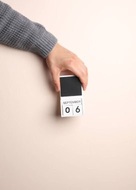 Süveter giymiş bir adamın elinde blok takvimi var. Bej arka planda 6 Eylül tarihi var.