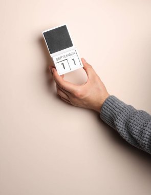 Süveter giymiş bir adamın elinde 11 Eylül 'ün bej arkaplanda olduğu blok takvimi var.