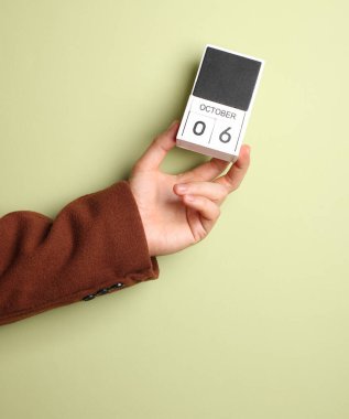 Ceketli adamın elinde blok takvimi var. Yeşil arka planda 6 Ekim tarihi var.