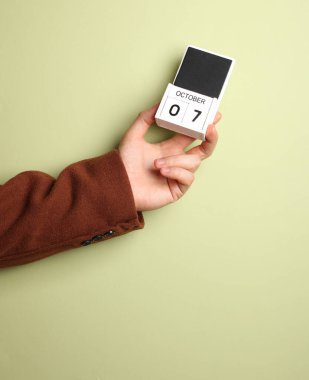 Paltolu adamın elinde blok takvimi var. Tarihi de 7 Ekim, yeşil arka plan.