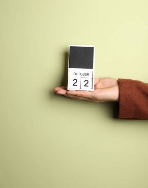 Ceketli adamın elinde blok takvimi var. Tarih 22 Ekim, yeşil arka plan.