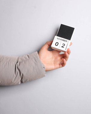 Ilık ceketli adamın eli, gri arkaplanda tarihi 2 Kasım olan blok takvimini tutuyor.