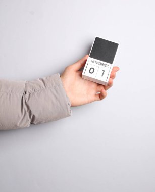 Ilık ceketli adamın eli blok takvimini tutuyor. 1 Kasım tarihli gri arkaplan.