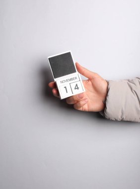 Ilık ceketli adamın eli, gri arkaplanda 14 Kasım tarihli blok takvimini tutuyor.