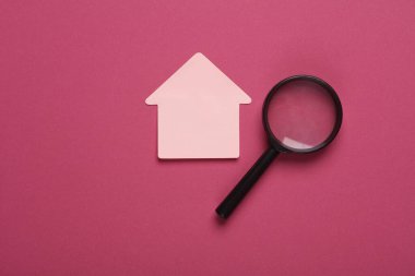 Pembe arka planda büyüteçle ev şeklinde not kağıdı.