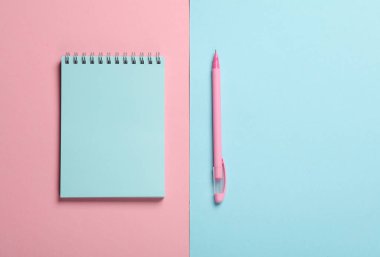 Mavi-pembe arka planda not defteri olan bir kalem. Pastel renk eğilimi