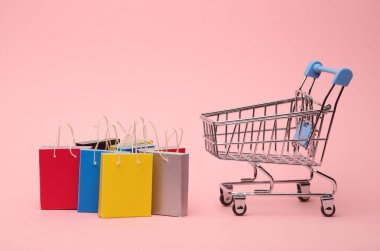 Pembe arka planda süpermarket tramvayında minyatür alışveriş çantaları. Kara Cuma, dünya alışveriş günü, indirim.