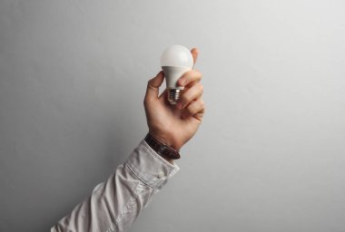 Beyaz gömlekli adamın elinde gri arka planda ampul var.