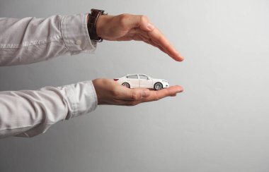 Beyaz gömlekli adamın elinde gri arka planda oyuncak araba var. Otomatik sigorta