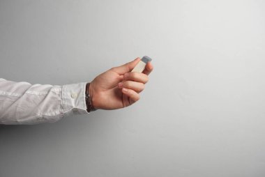 Beyaz gömlekli adamın eli gri arka planda silgi taşıyor.