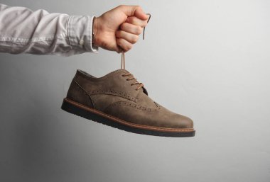 Beyaz gömlekli adamın elinde gri arka planda parlak ayakkabılar var..