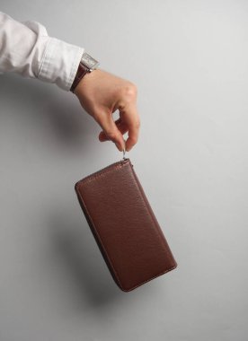 Beyaz gömlekli adamın eli gri arka planda deri çanta taşıyor.