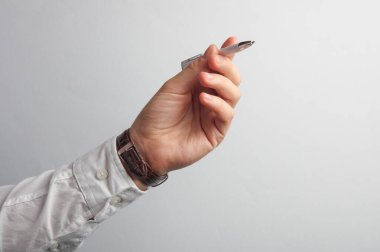 Beyaz gömlekli adamın eli gri arka planda kalem tutuyor. İş konsepti