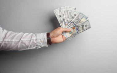 Beyaz gömlekli bir erkek. Gri arka planda 100 dolarlık banknotlar tutuyor.