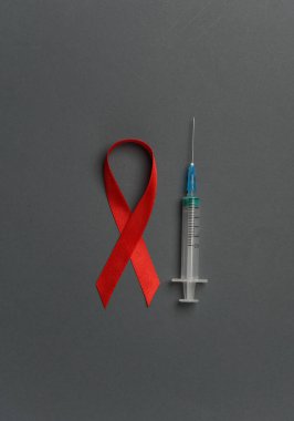 Koyu arkaplanda şırınga olan kırmızı farkındalık kurdelesi. Dünya HIV Yardım Günü 