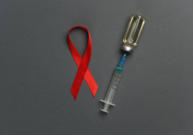 Siyah arka planda şırınga ve aşı şişesiyle kırmızı farkındalık kurdelesi. Dünya HIV Yardım Günü 