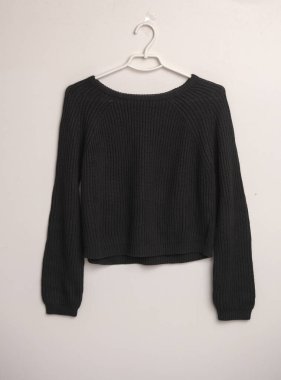 Beyaz arka planda askısı olan siyah kadın yün süveteri.