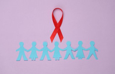 Kağıt kesiği insan zinciri ve mor arka planda kırmızı farkındalık kurdelesi. Birlik, destek, birlikte daha güçlüyüz. Dünya HIV Yardım Günü 
