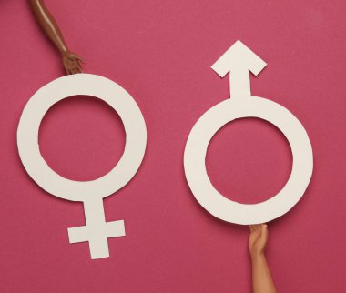 Pembe arka planda kadın ve erkek cinsiyet sembolleri tutan bebekler. Cinsiyet eşitliği