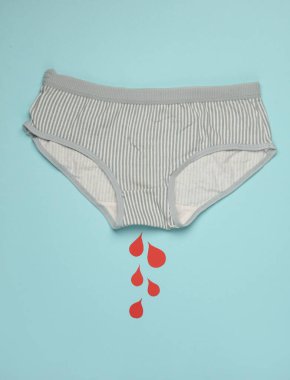 Üzerinde kağıt olan külotlar mavi arka planda kan damlalarını kesiyor. Kritik Kadın Günleri