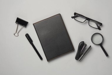 Not defteri, zımba, gözlük, klasör, gri arka planda büyüteç. Siyah kırtasiye eşyaları