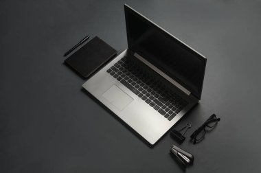 Koyu gri arka planda dizüstü bilgisayar, defter ve kırtasiye malzemeleri. İş konsepti. Yaratıcı yerleşim