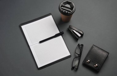 Defter ve çanta, kahve fincanı, gözlükler, koyu gri arka planda zımba. İş konsepti. Üst Manzara. Düz yatıyordu