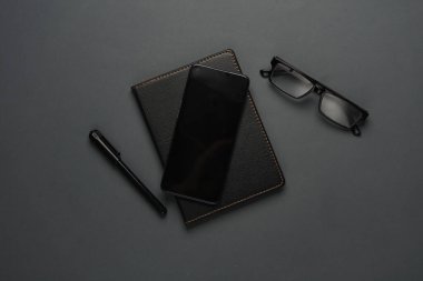 Deri not defteri, arka planda akıllı telefon, kalem ve gözlük. Üst görünüm