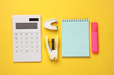 Sarı arka planda hesap makinesi ve okul kağıtları. Şişko karı. Üst görünüm