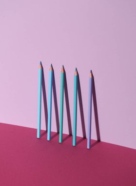 Pembe arka planda gölgeli mavi renkli kalemler. Yaratıcı yerleşim