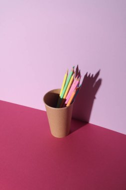 Pembe arka planda, fincanda renkli kalemler. Yaratıcı yerleşim