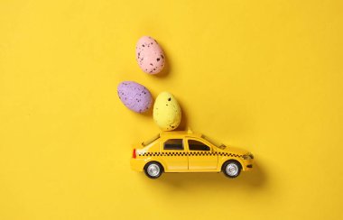 Sarı arka planda Paskalya yumurtaları olan oyuncak taksi modeli..