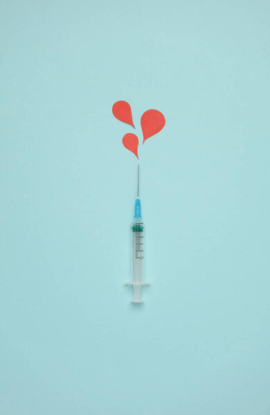 Syringe and paper-cut blood drops on blue background