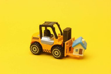 Minyatür oyuncak forklift ve sarı arka planda bir ev. Ev alınıyor
