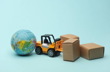 Mavi arka planda kutuları olan minyatür bir forklift ve küre. Lojistik, ulaşım, teslimat