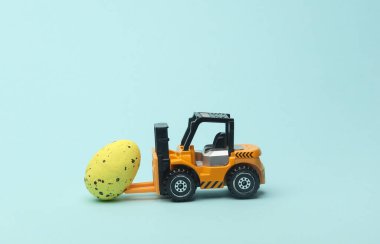 Minyatür oyuncak forklift ve mavi arka planda Paskalya yumurtası..