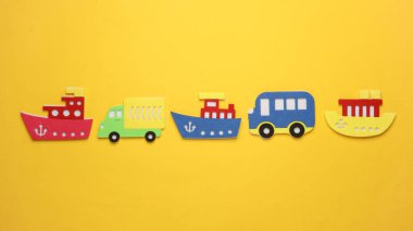 Oyuncak otobüsler ve kamyonlar, sarı arka planda keçeden gemiler..