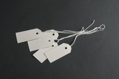 Koyu gri arka planda ipleri olan boş beyaz etiketler. Tasarım için şablon oluşturun. Uzayı kopyala Satış, alışveriş konsepti