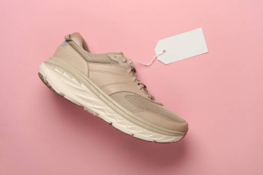 İp üzerinde beyaz boş etiketli, pembe arka planlı bir koşu ayakkabısı. Tasarım, satış ve alışveriş için şablon