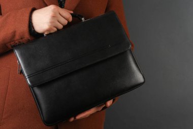 Koyu gri arka planda yün ceketli bir adam evrak çantasını tutuyor.