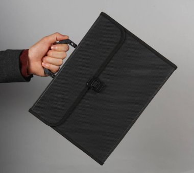 Gri arka planda siyah plastik bir evrak çantası tutan bir erkek.