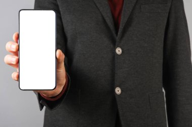 Gri arka planda akıllı telefonu tutan ceketli bir iş adamı.
