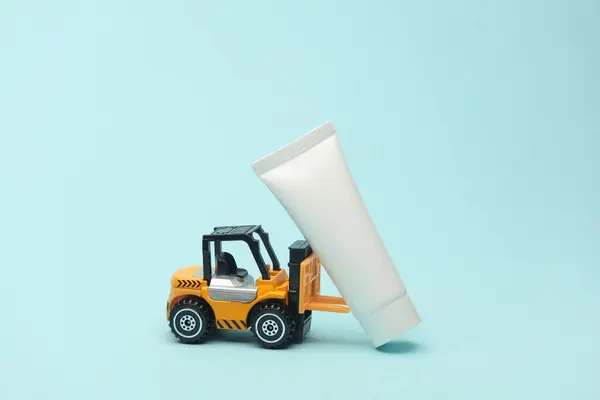 stock image Miniature toy forklift and cream tube on blue background. Beauty concept