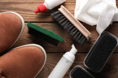 Ahşap bir arka planda ayakkabı bakım ürünleri ve aksesuarlı süet ayakkabılar.